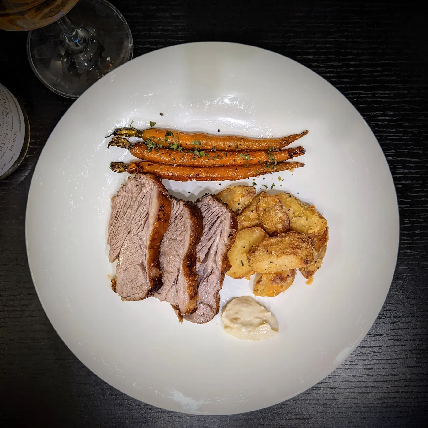Home-cooked Sunday roast with sliced lamb, roasted carrots and crispy potatoes on a white plate